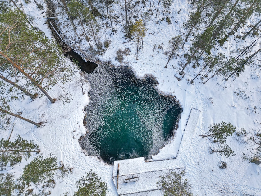 an aerial view of a snow covered lake surrounded by trees