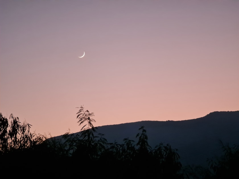 the moon is setting in the sky over the mountains