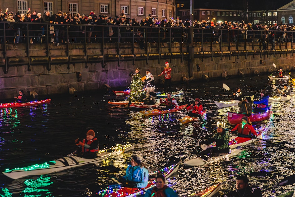 People in illuminated kayaks parade on a canal at night.