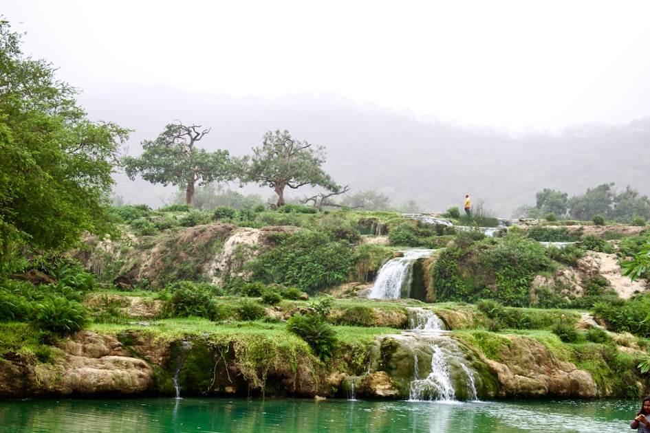 a man standing in the water next to a waterfall