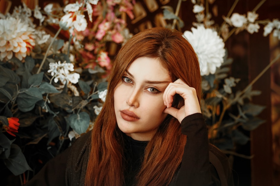 a woman with long red hair holding her hand to her face